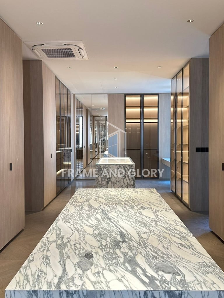 Modern kitchen interior with marble countertop, wooden cabinetry, and glass-fronted storage units under recessed ceiling lights