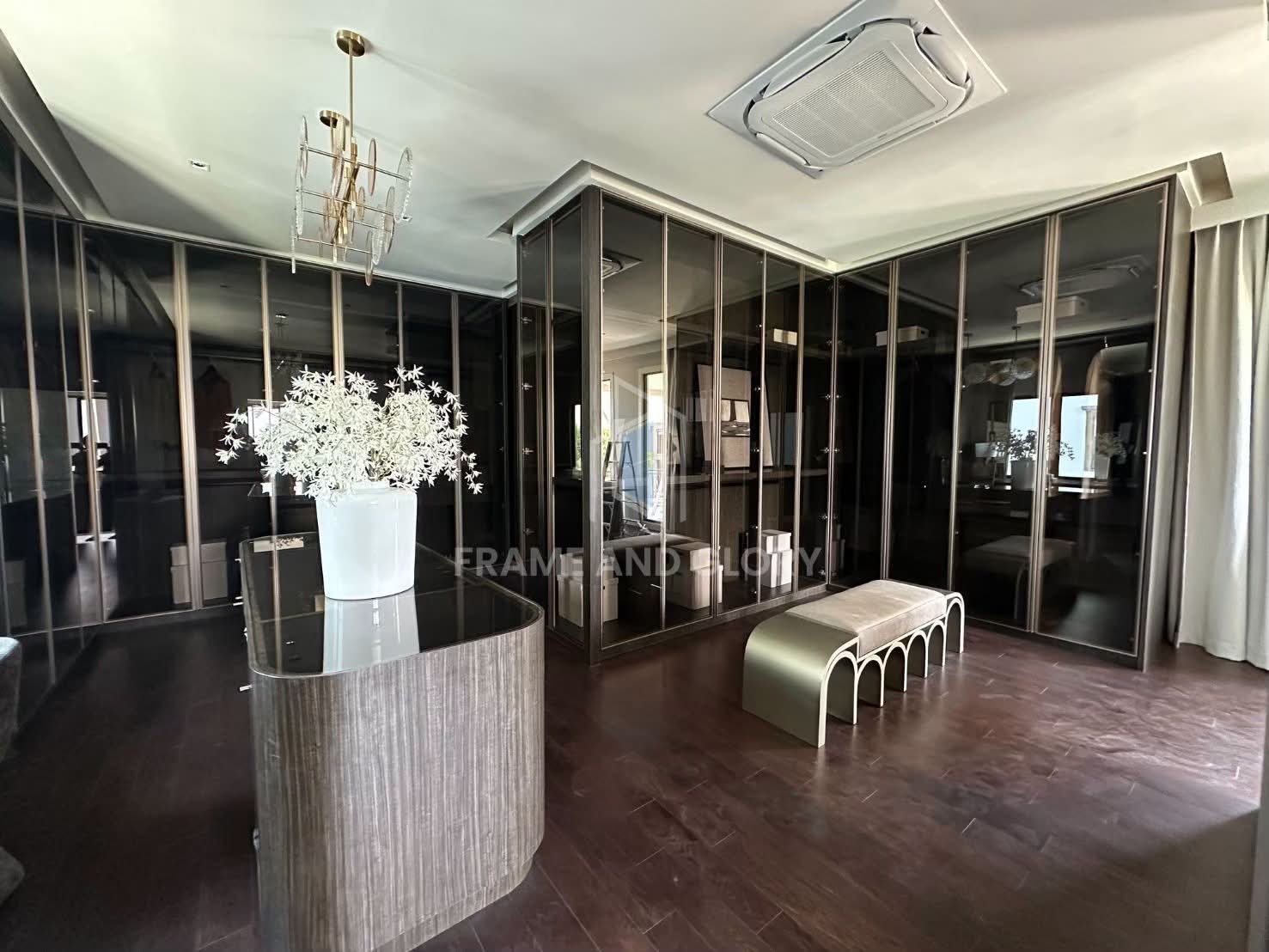 Modern showroom with black-framed glass partitions, dark wooden flooring, white flower arrangement on pedestal, and contemporary furniture display
