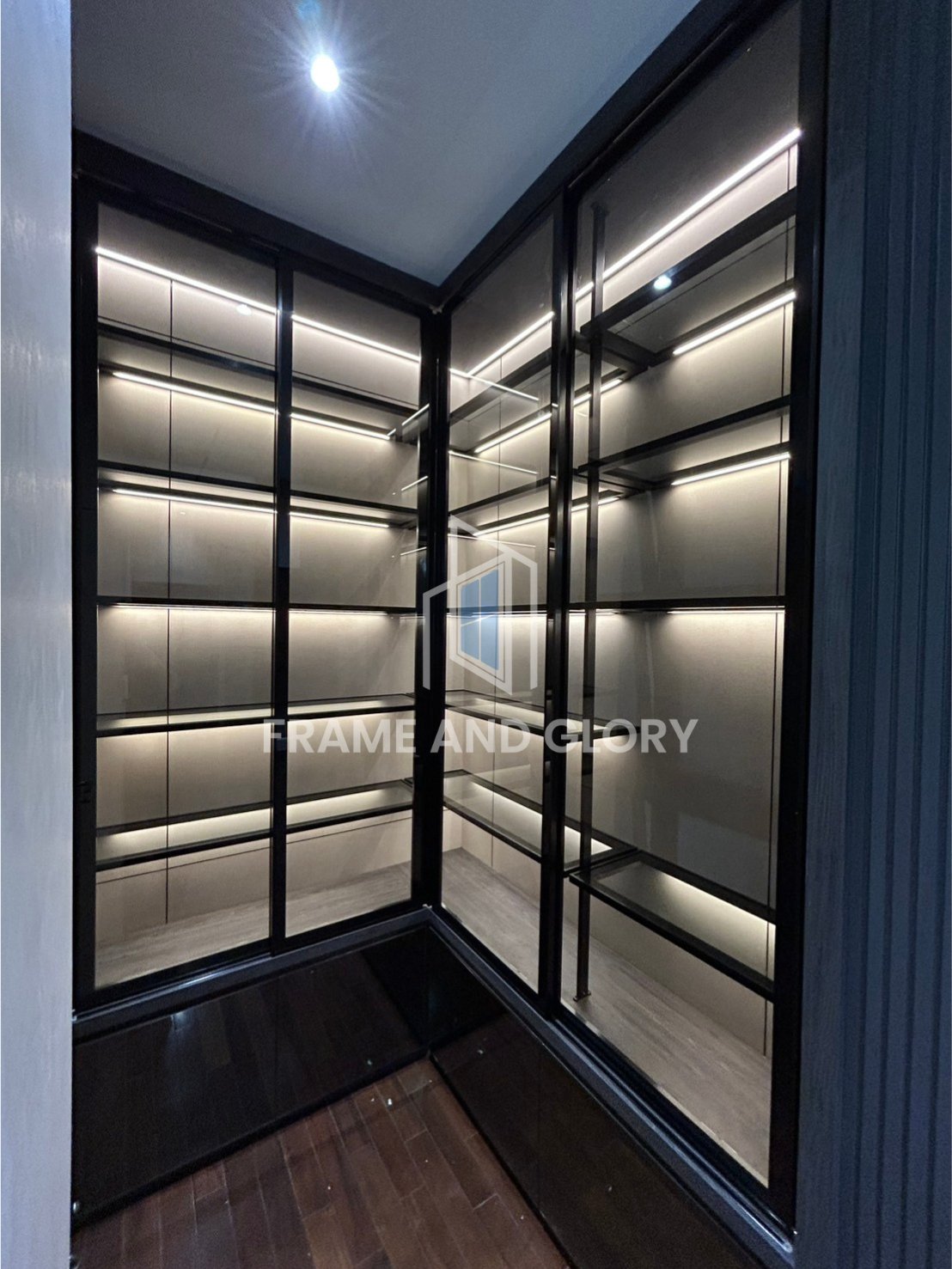 Modern corner display cabinet with black metal frame, glass doors, interior LED lighting, and empty shelves