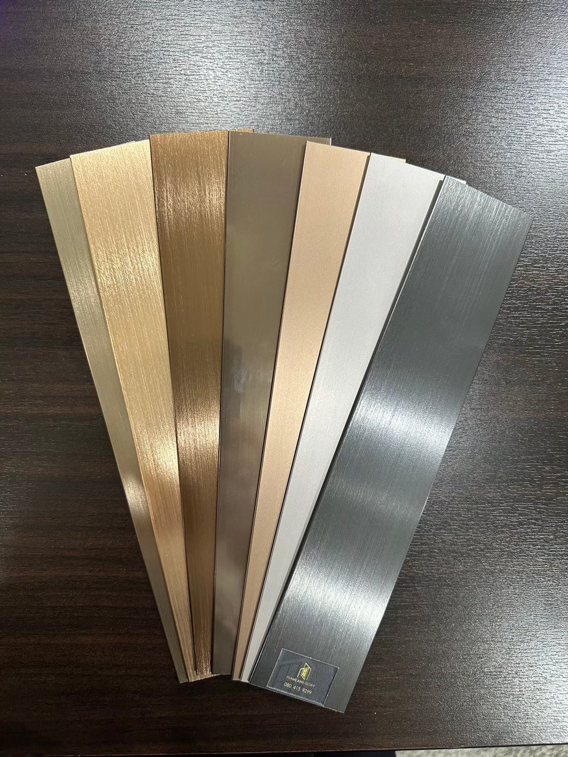 Seven material samples fanned out showing wood grain and metallic finishes in various colors from light to dark